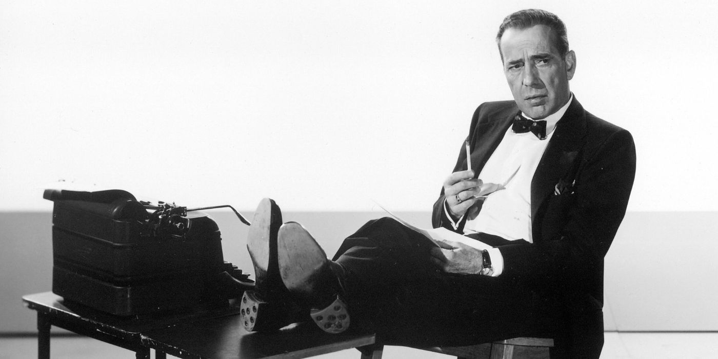 Humphrey Bogart sitting on a chair with his legs leaning on a table against a typewriter in The Harder They Fall
