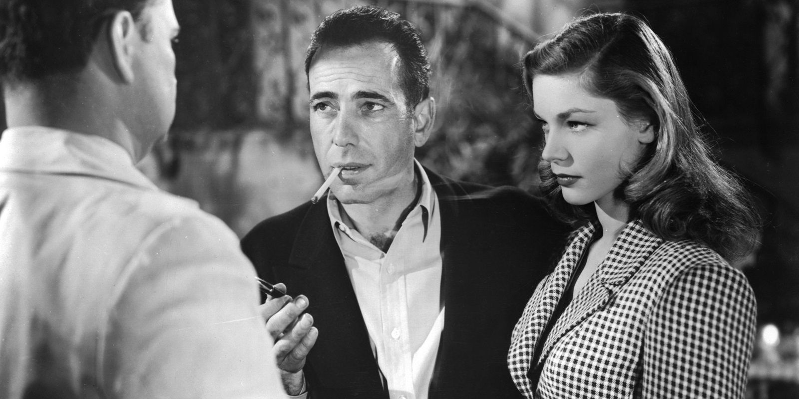 Humphrey Bogart smoking a cigarette while Lauren Baccall looks sideways in To Have and Have Not