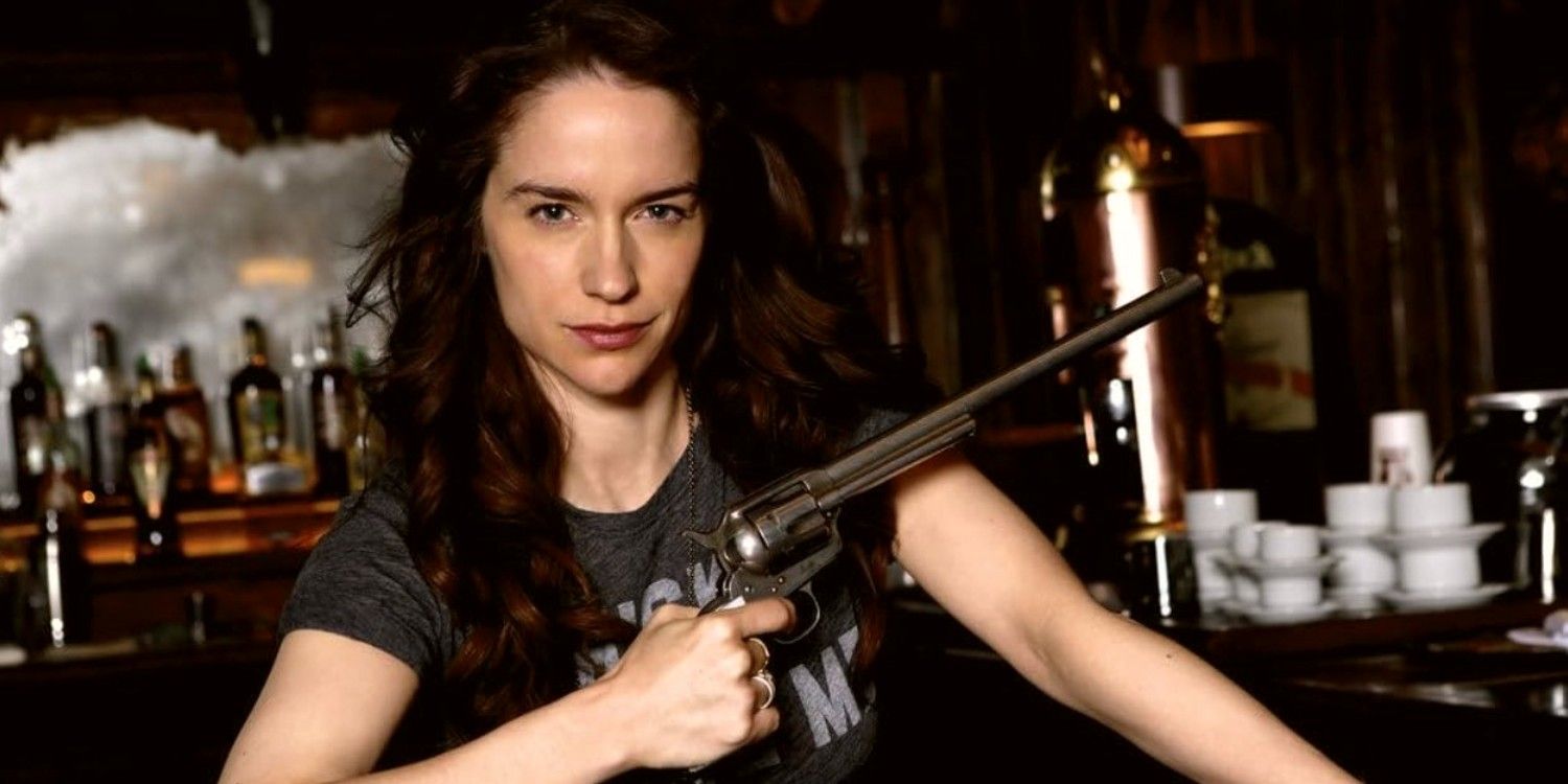 Melanie Scrofano sentada en un bar con Peacemaker en Wynonna Earp