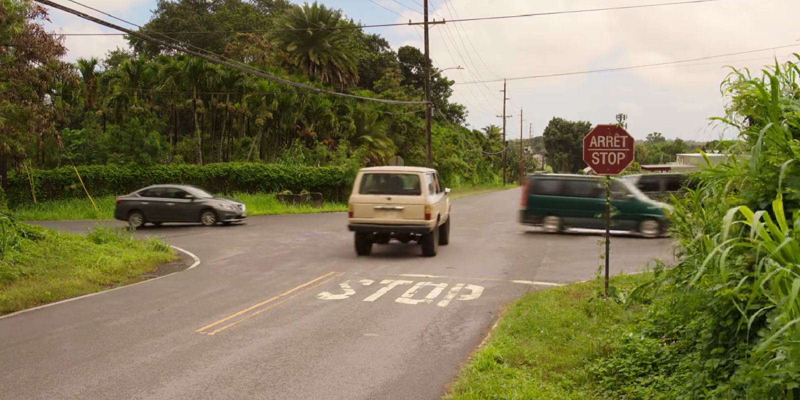 A car drives through a stop sign almost hitting two other vehicles.