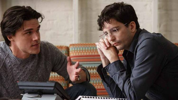 Finn Wittrock as Jamie Shipley and John Magaro as Charlie Geller staring at a phone in The Big Short.