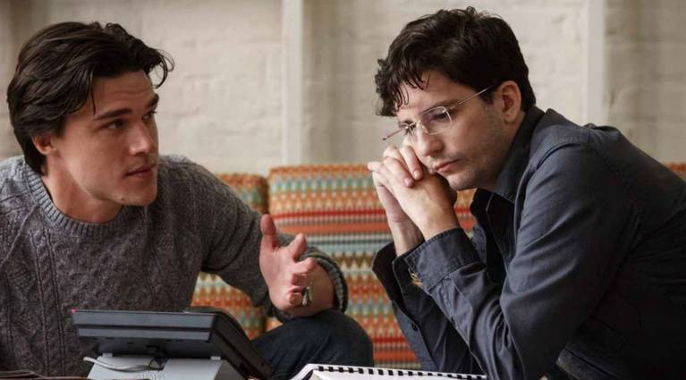 Finn Wittrock as Jamie Shipley and John Magaro as Charlie Geller staring at a phone in The Big Short.