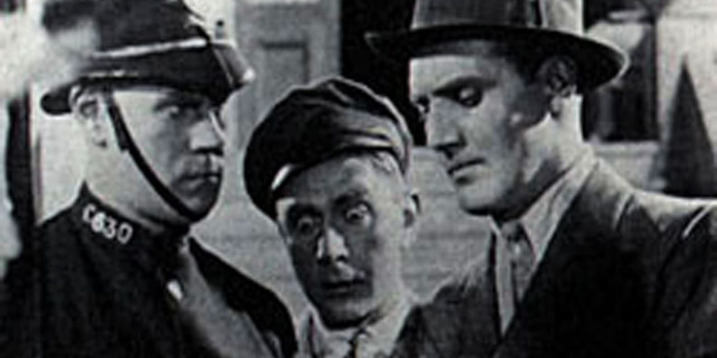 A police officer talks to a man in a suit while a third person looks shocked.