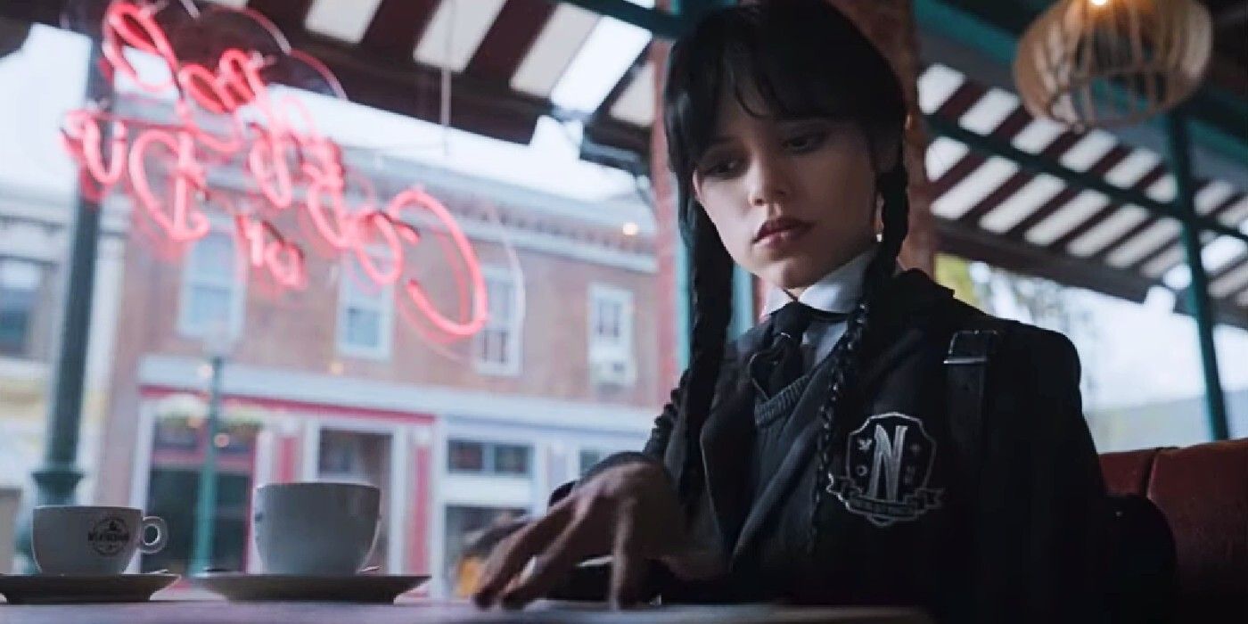Wednesday Addams (Jenna Ortega) looking down at a pamphlet while sitting at the Weathervane coffee shop in Wednesday.