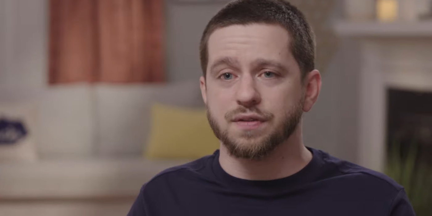 Clayton 90 Day Fiance talking to cameras blurred background dark shirt