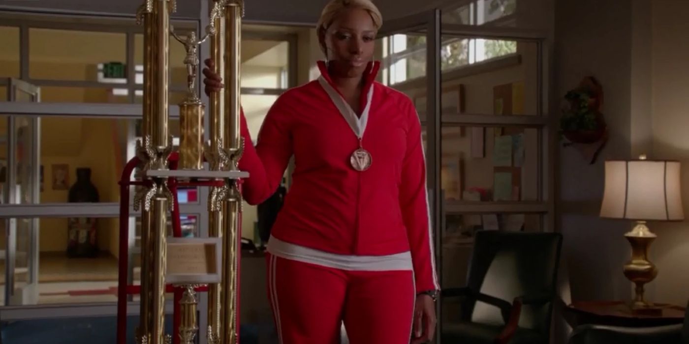 Coach Roz holds a giant trophy while wearing a red track suit.