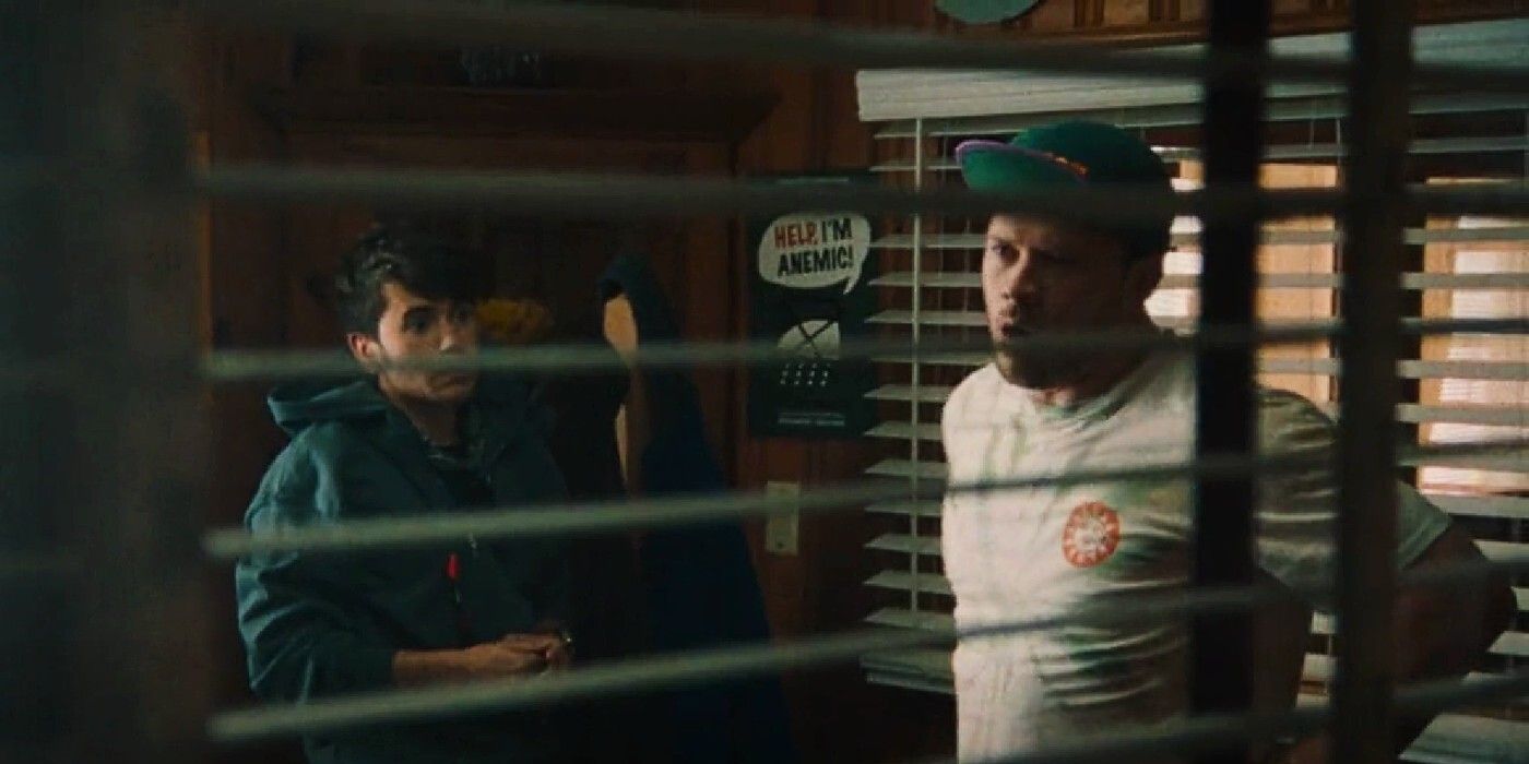 Glenn and Troy talk in a room behind some blinds in a scene from Theater Camp.