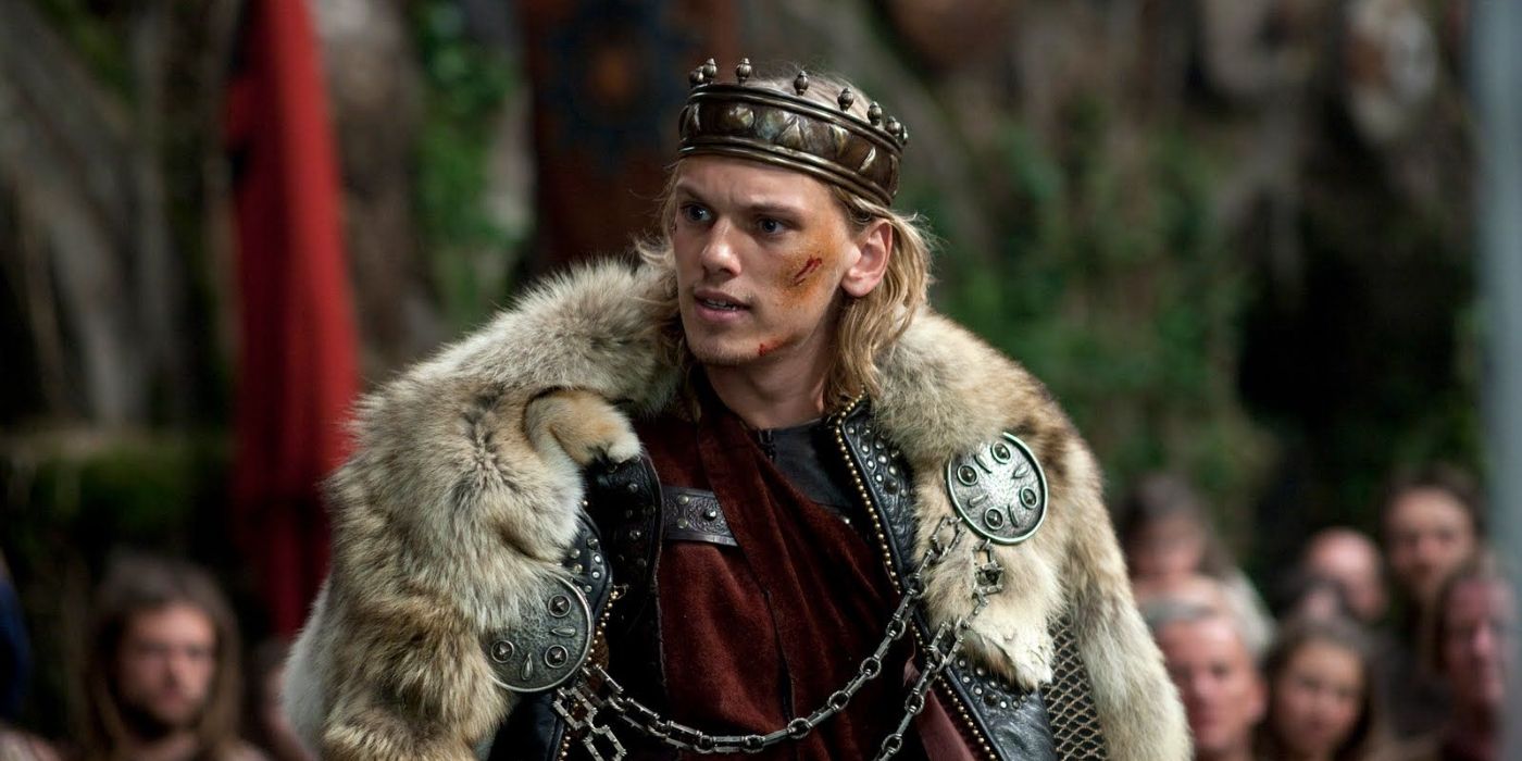 Jamie Campbell Bower como Rei Arthur com cicatrizes em um casaco em Camelot