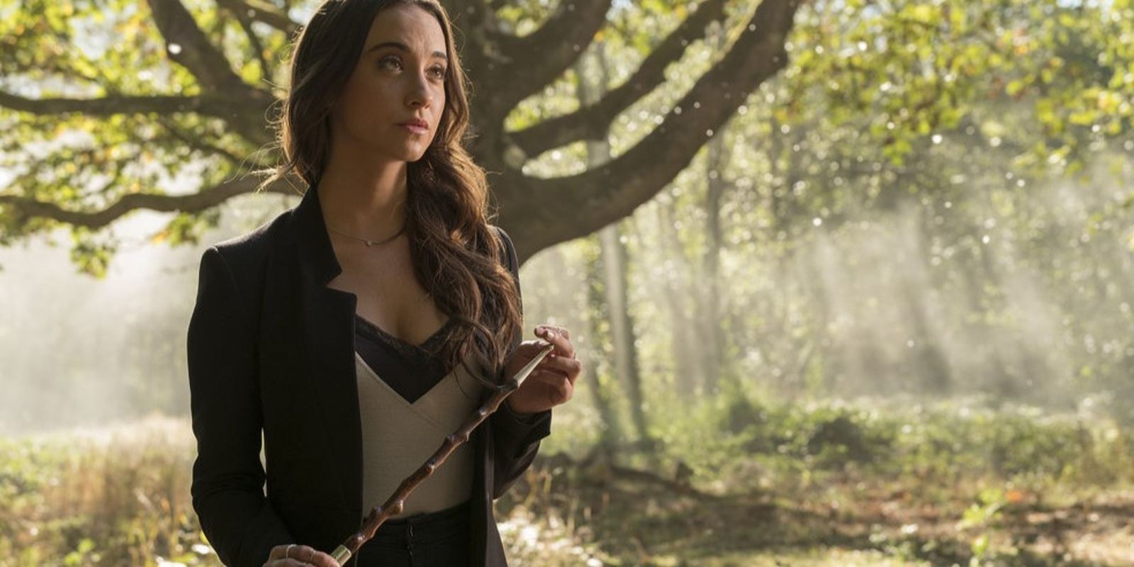 Julia segura a varinha do bruxo enquanto está na floresta.