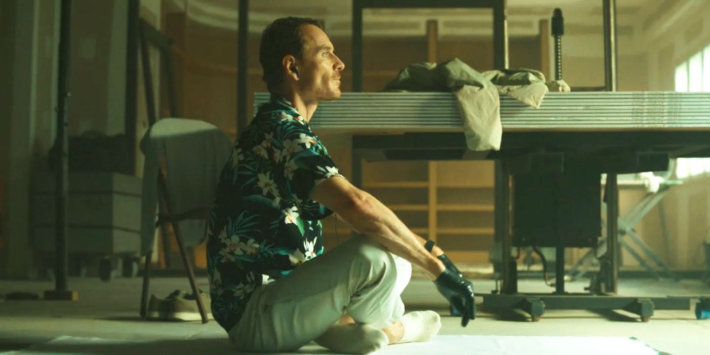 Michael Fassbender as the Killer, sitting crosslegged on the ground in The Killer