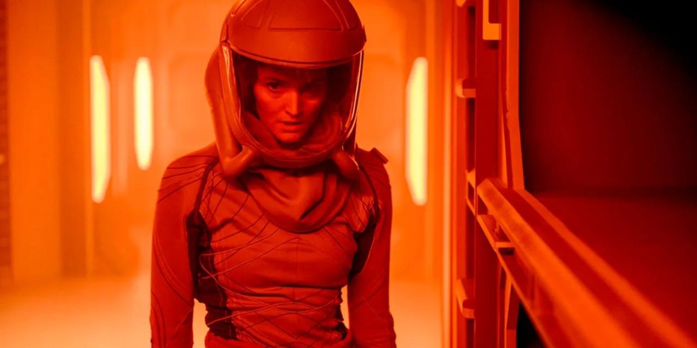 Sharon wears a space helmet and walks through a red corridor in The Ark