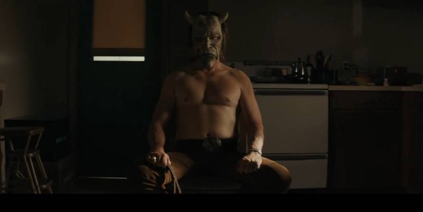 The Grabber (Ethan Hawke) sitting shirtless in a dark room in The Black Phone.