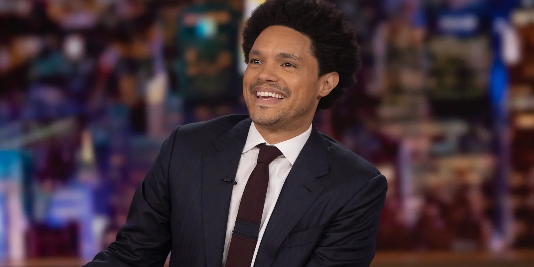 Trevor Noah smiling while hosting The Daily Show on Comedy Central