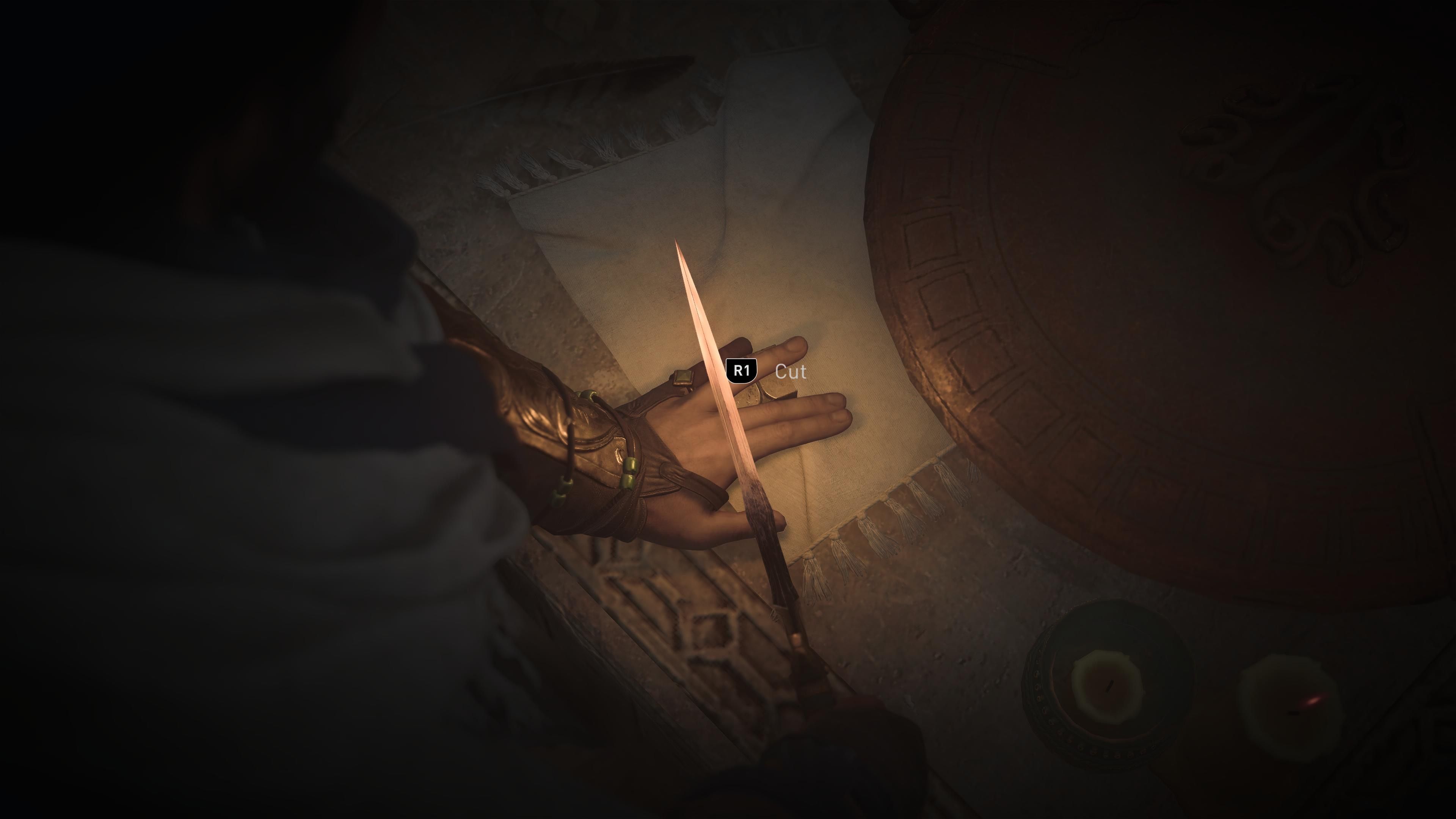 A hand is illuminated in a dark scene, with the ring finger resting on an object above the others. Held above the ring finger is a knife, accompanied by an R1 button prompt and text that says, 