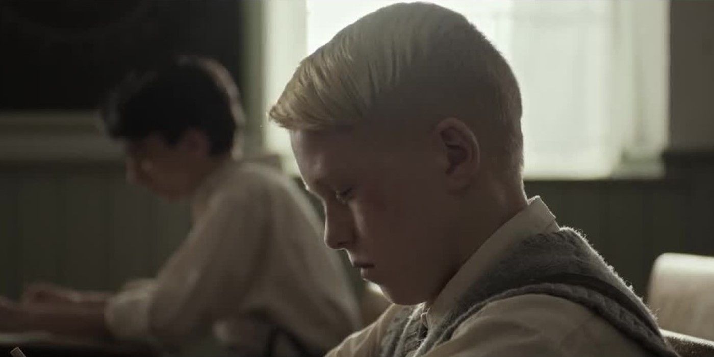 A young boy in school looking down sadly at his desk in Forgive Us Our Trespasses