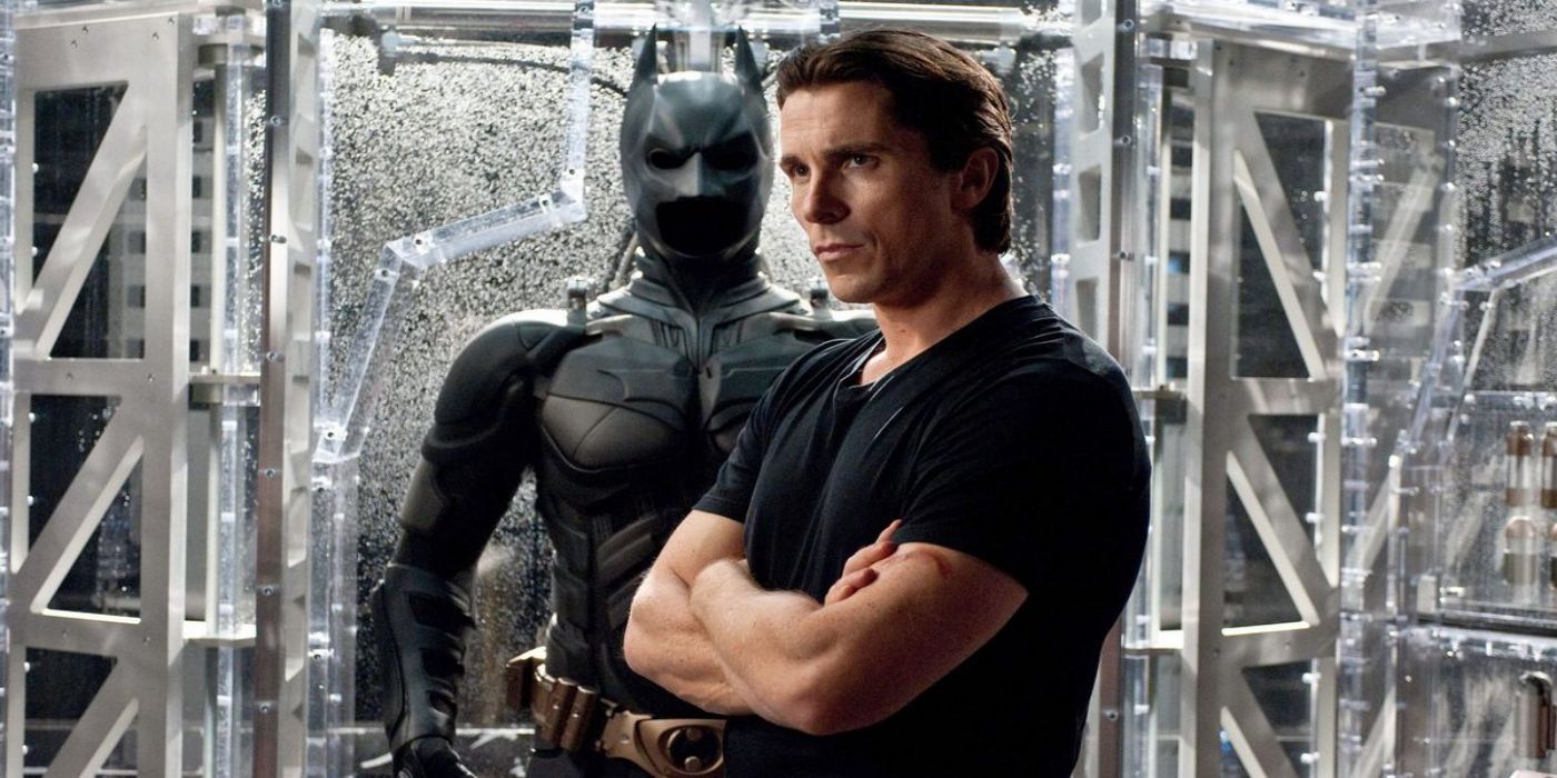 Christian Bale as Bruce Wayne stands in front of his Batman suit in The Dark Knight