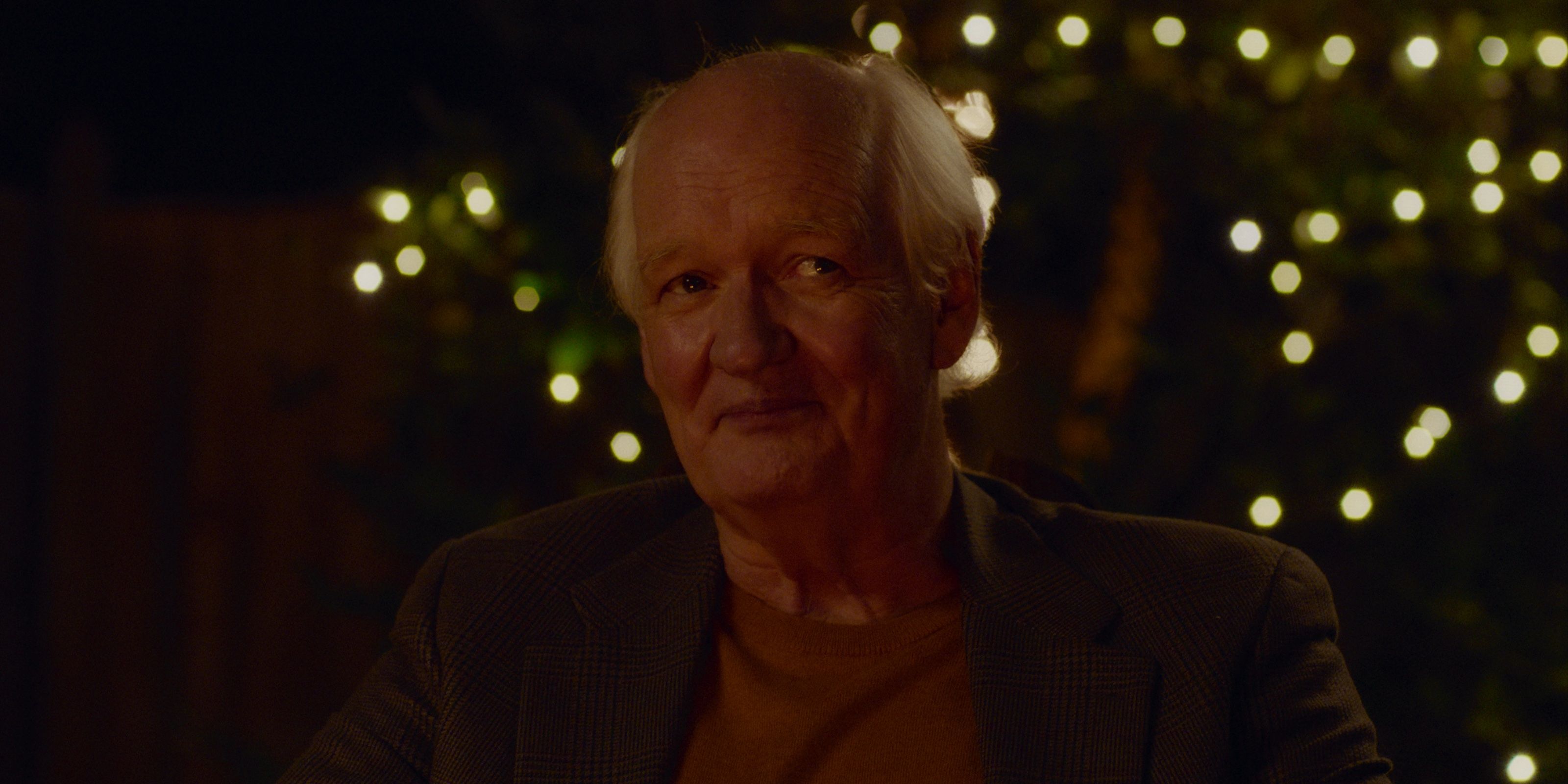 Colin Mochrie in How To Ruin The Holidays with Christmas lights in the background.
