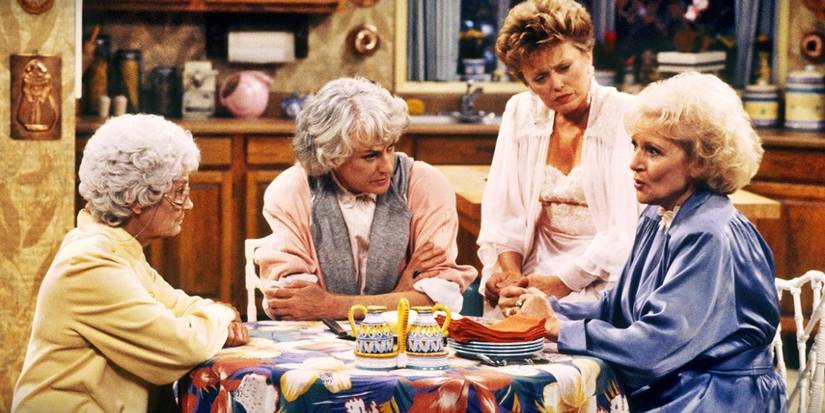 Sophia, Dorothy, Blanche, and Rose in their pajamas and robes at the kitchen table in Golden Girls