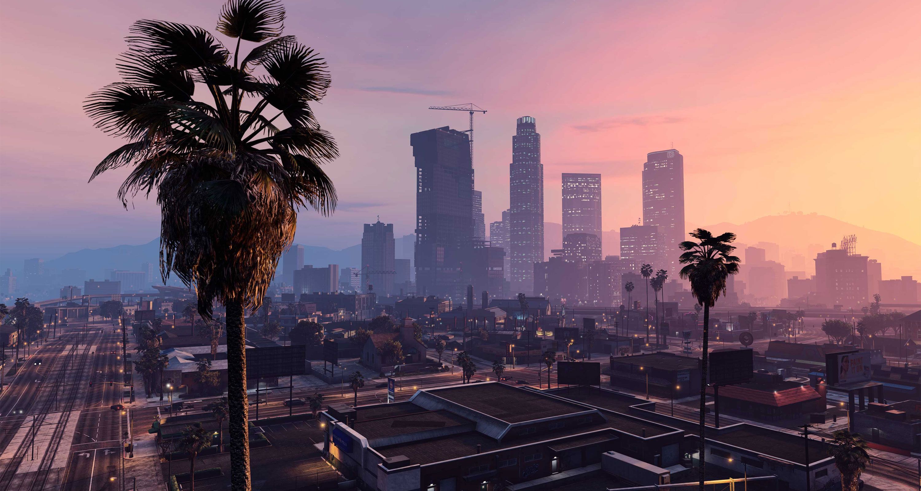 A palm tree blowing in the wind with a city during sunset in the background.