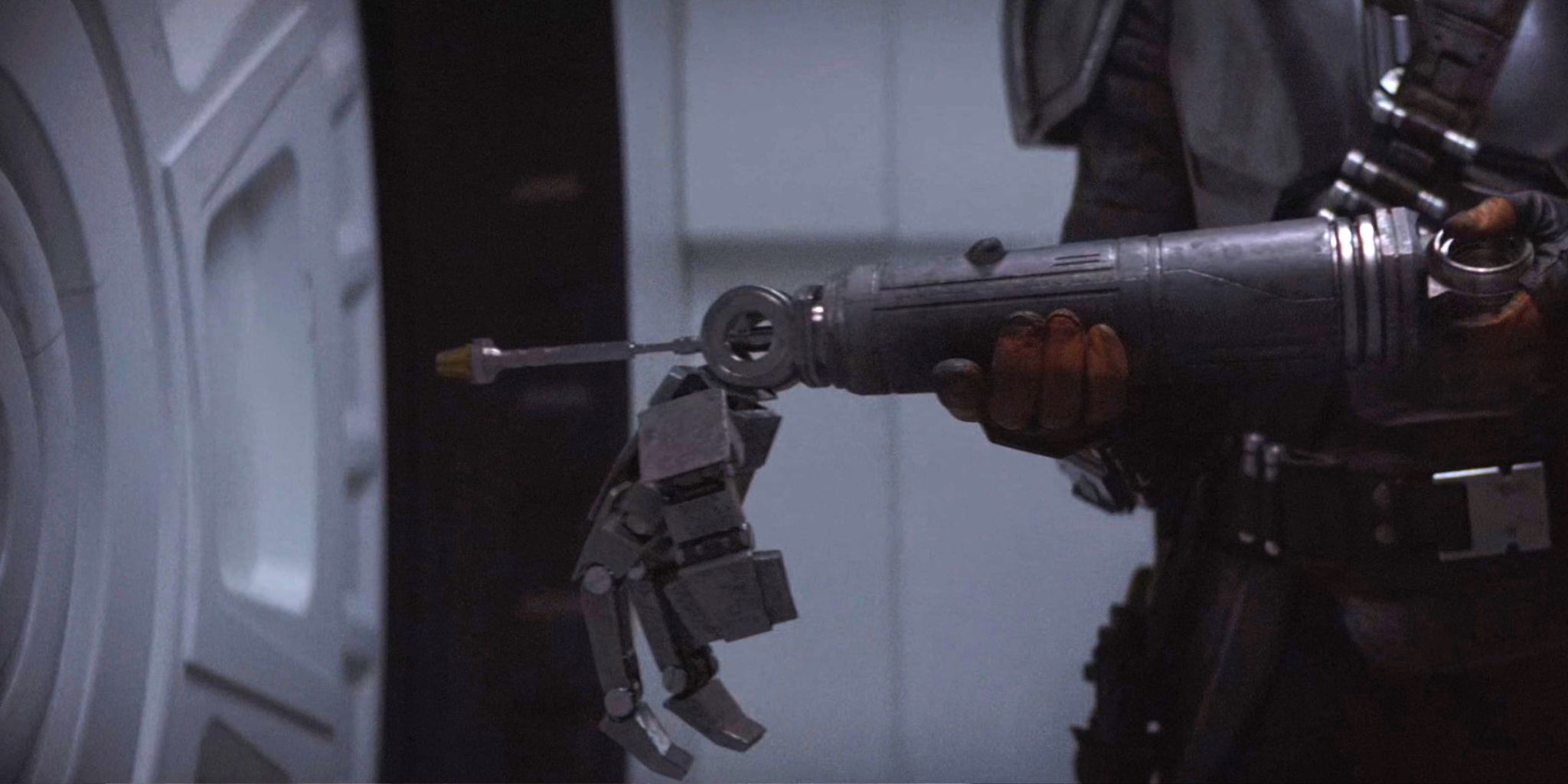 Din Djarin holds the broken arm of a New Republic security droid to unlock the door in The Mandalorian