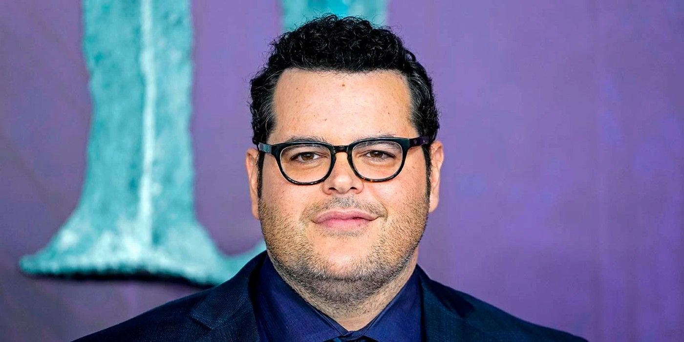 O ator e cantor Josh Gad sorri usando óculos e terno