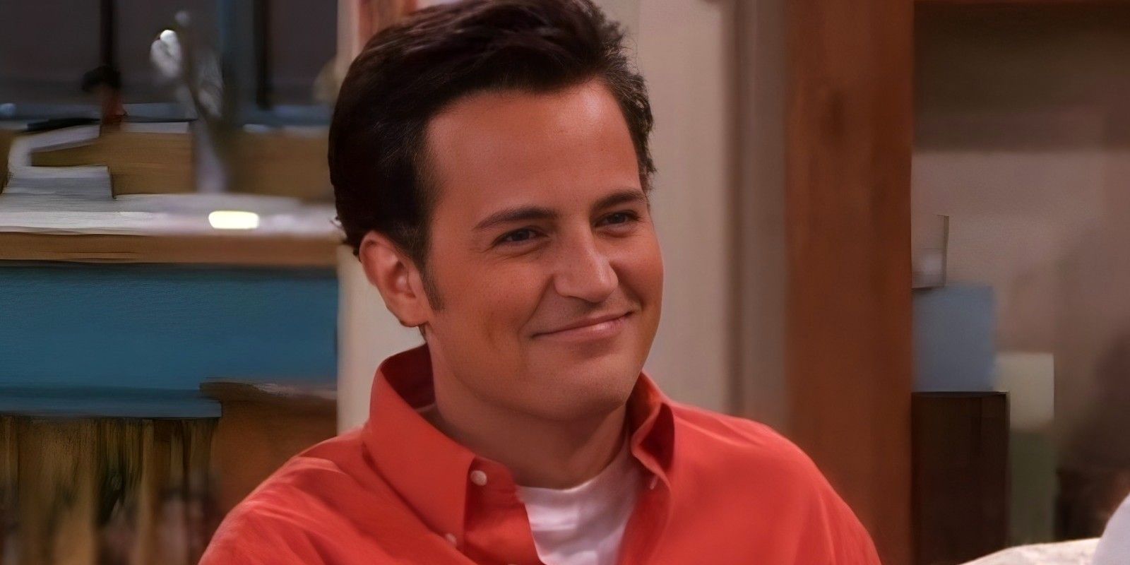 Chandler sorri enquanto está sentado em seu apartamento.