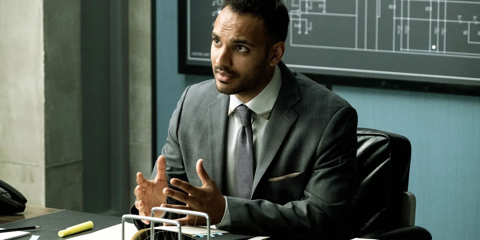 Penny sits at his desk talking to a student.