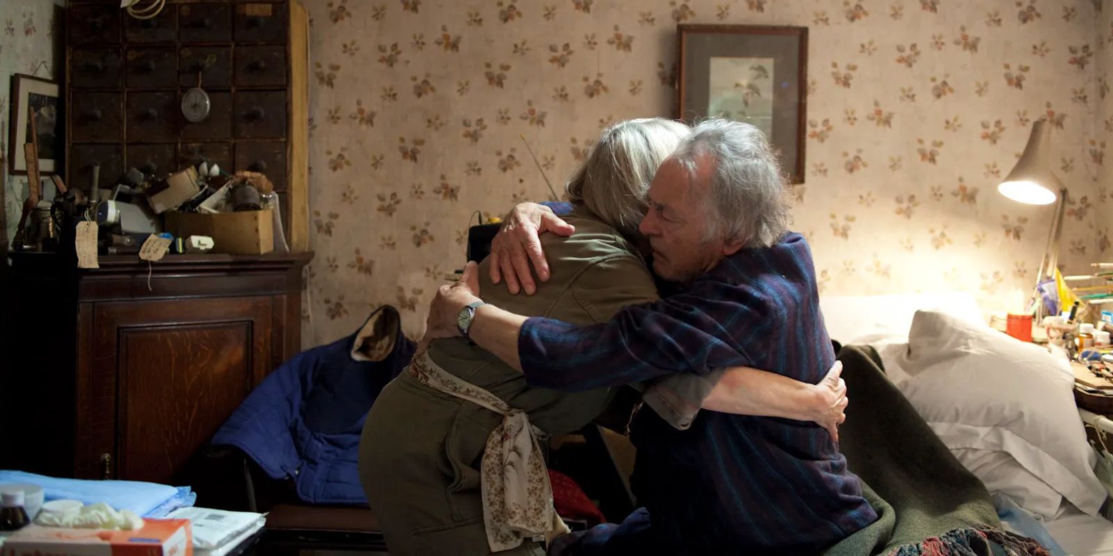 An elderly couple hugs in their bedroom.