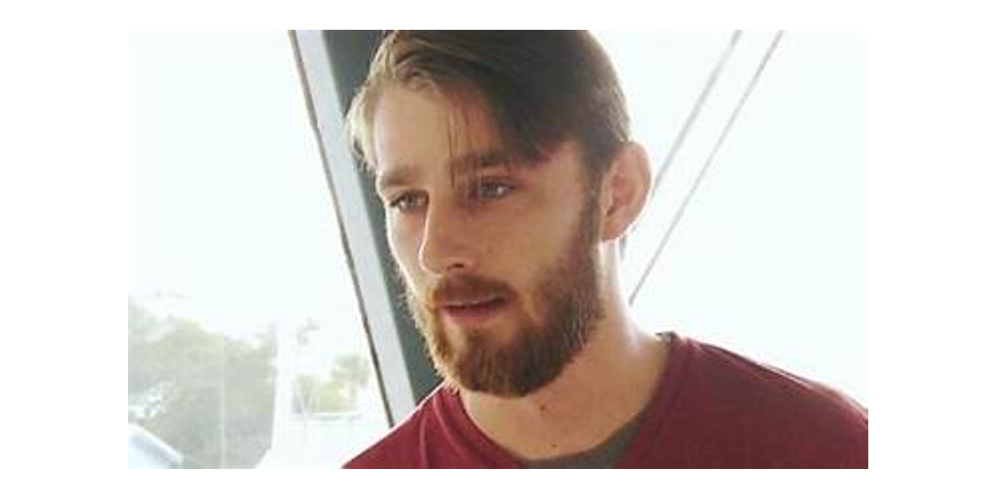 Kyle Dixon below deck in a red shirt, talking in front of a large window