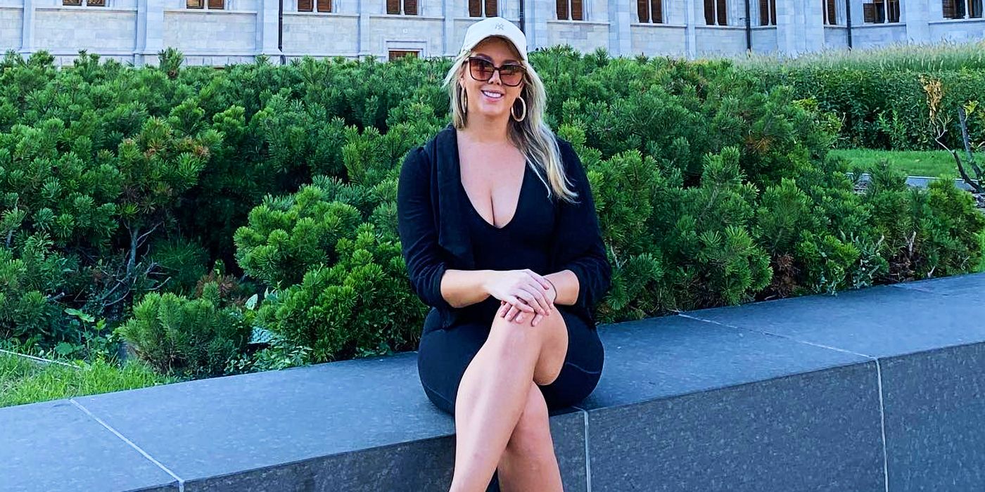 90 Day Fiance star Cortney Reardanz wearing black dress sitting on wall and smiling