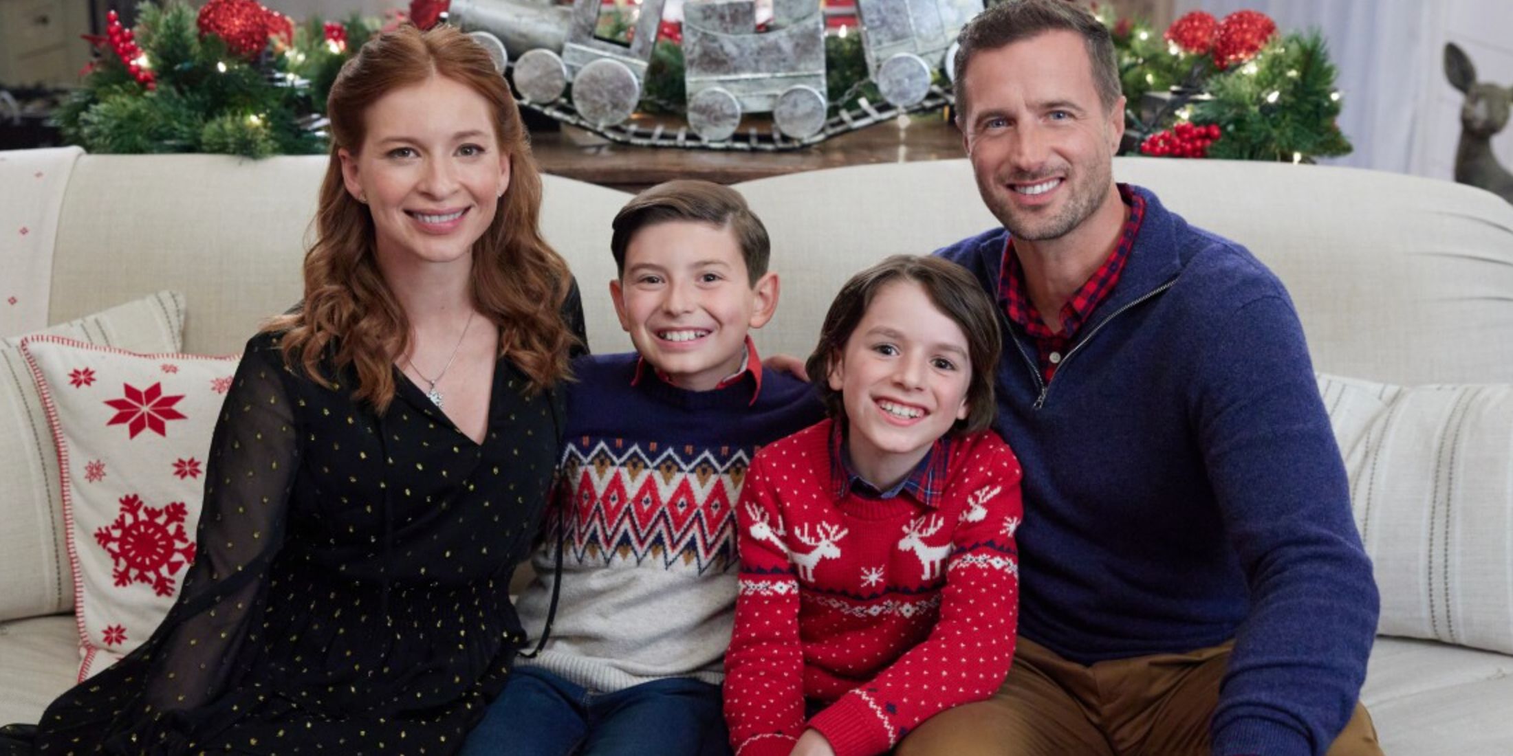 A woman and a man sit on a white couch with two young boys in the Hallmark movie A Season For Family