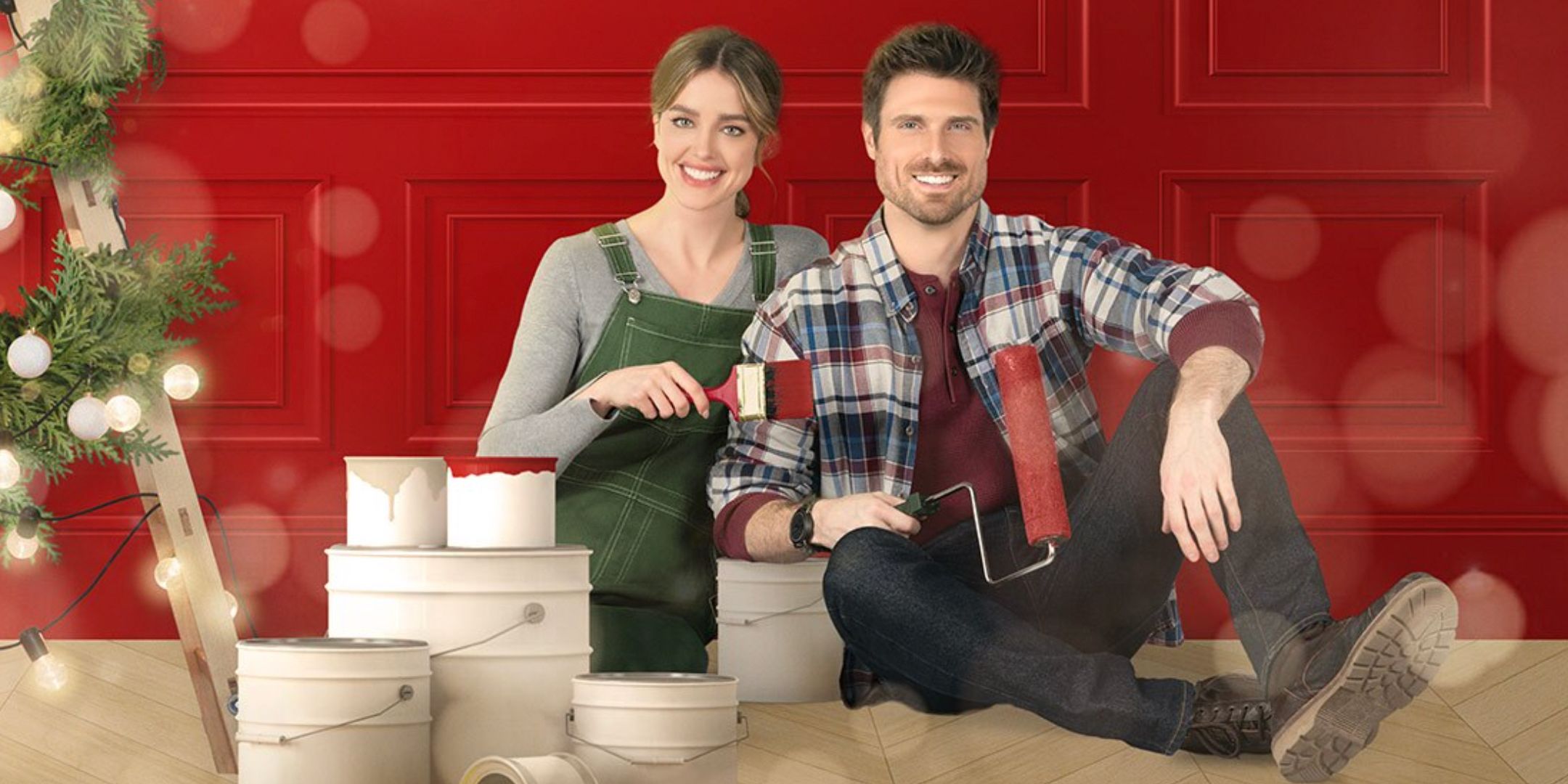 A woman and man sitting with paint cans and paint brushes in front of a red wall for Flipping Christmas
