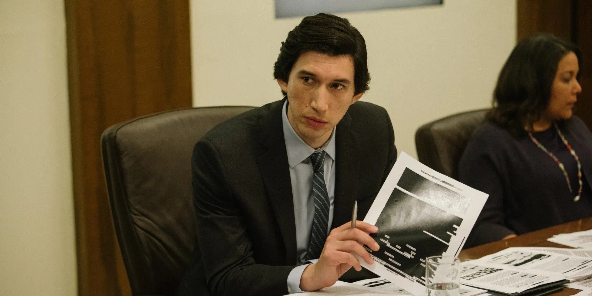 Adam Driver at a conference table, holding a heavily redacted document in The Report