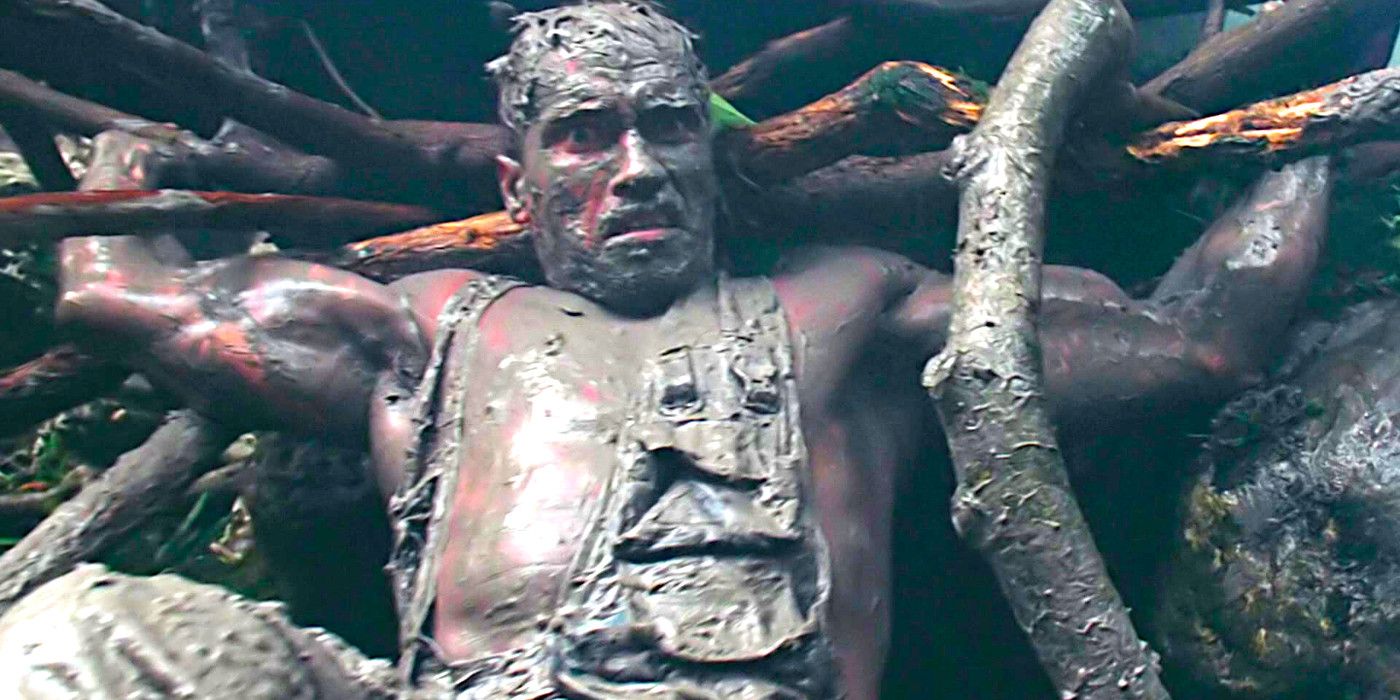 Arnold Schwarzenegger caked in mud and hiding from the alien in Predator