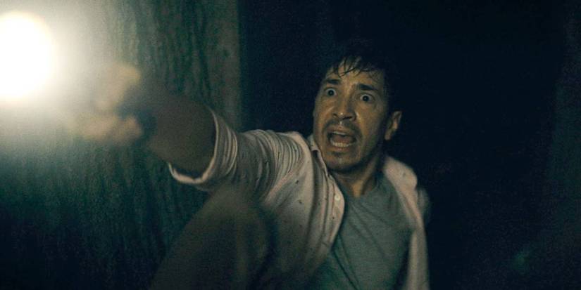 Justin Long looking scared and shining a flashlight in Barbarian