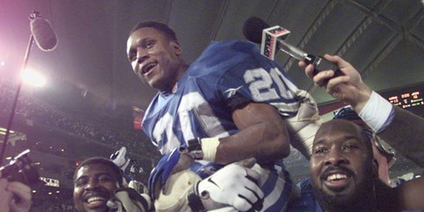 Barry Sanders held up inside a football stadium with microphones around him