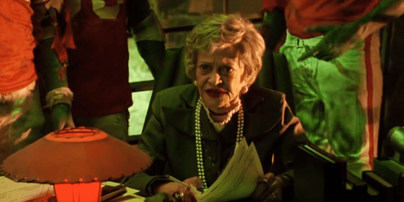 Juno (Sylvia Sidney) going through paperwork with the football players behind her in her office in Beetlejuice