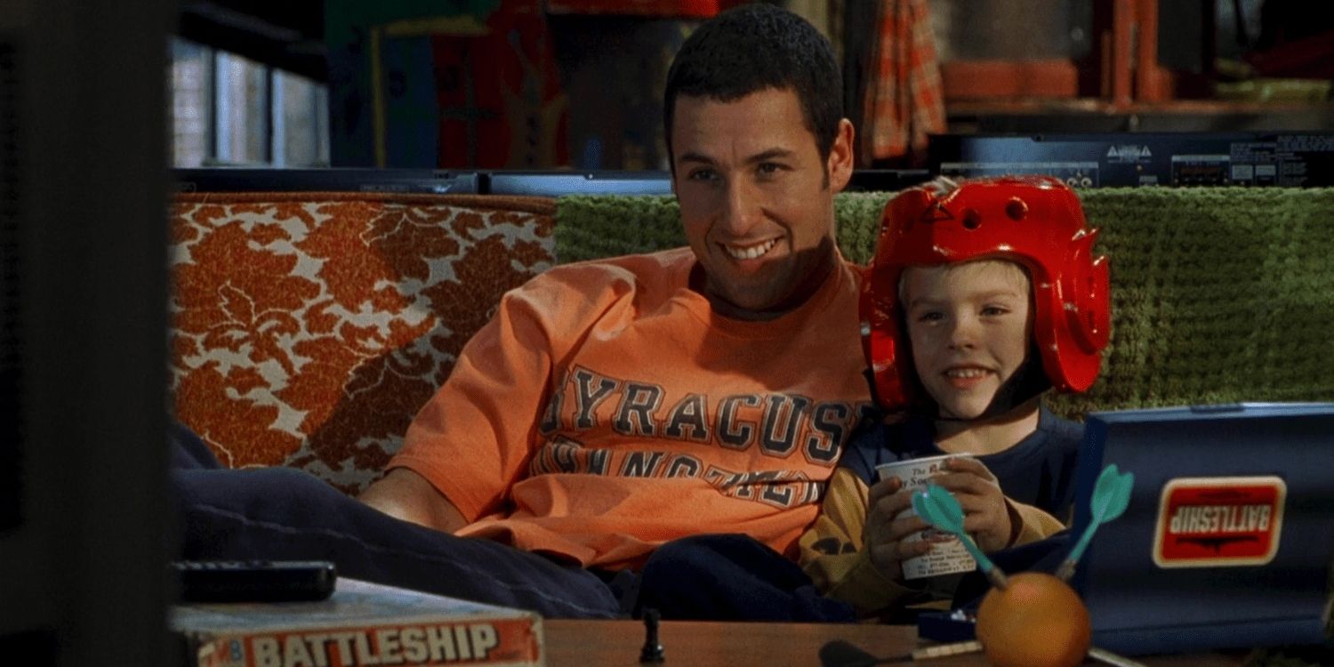 Sonny (Adam Sandler) e Julian (Cole Sprouse) sentados no sofá com um capacete em Big Daddy