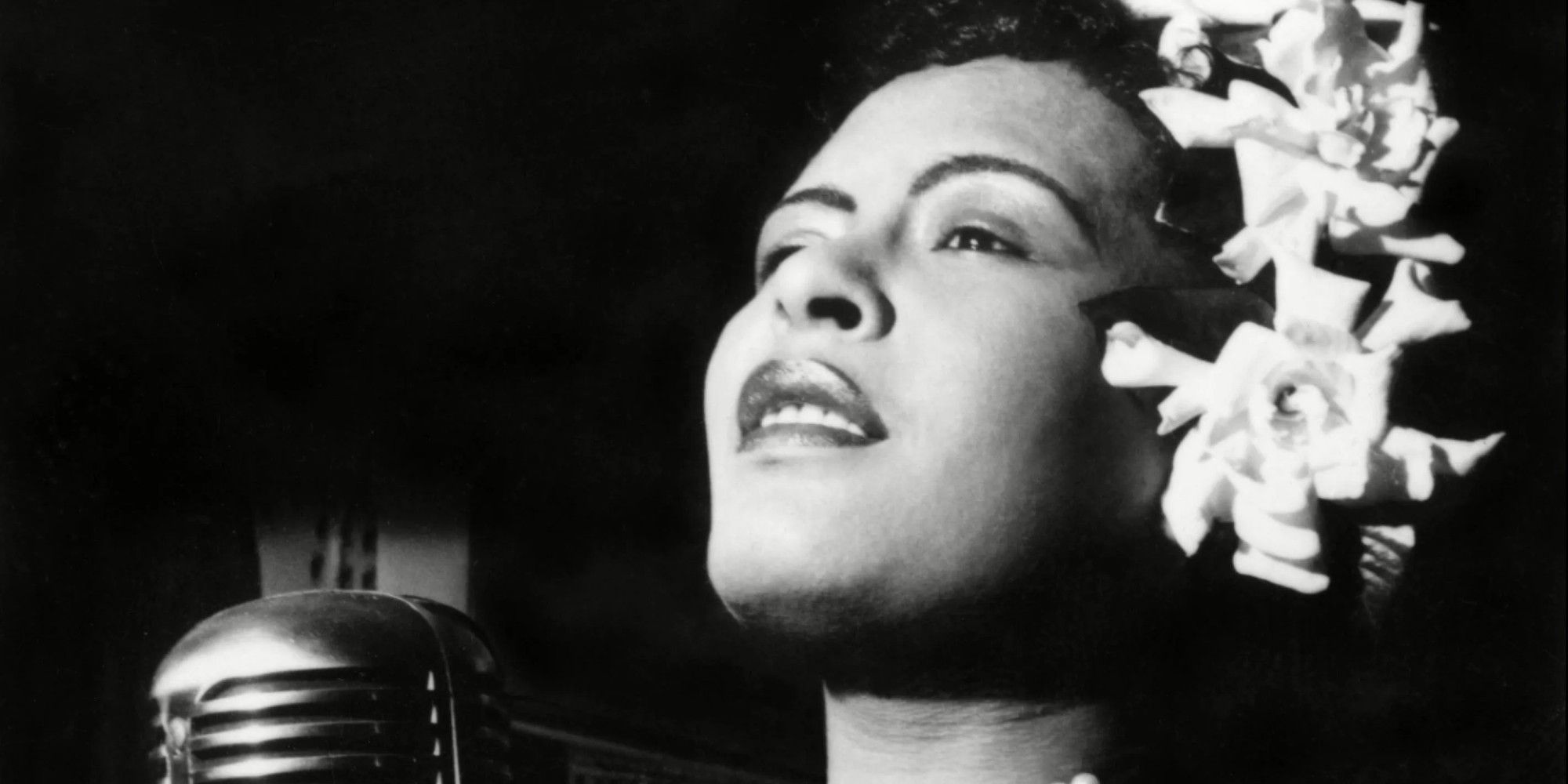 Billie Holiday singing into a microphone in black-and-white