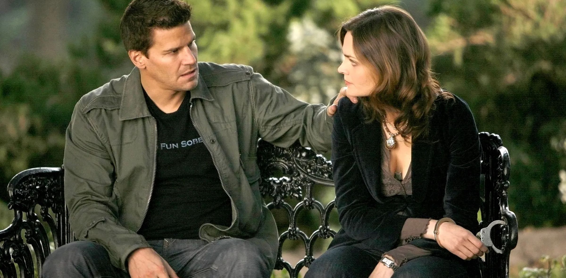 Brennan handcuffed to a park bench while Booth talks to her in Bones