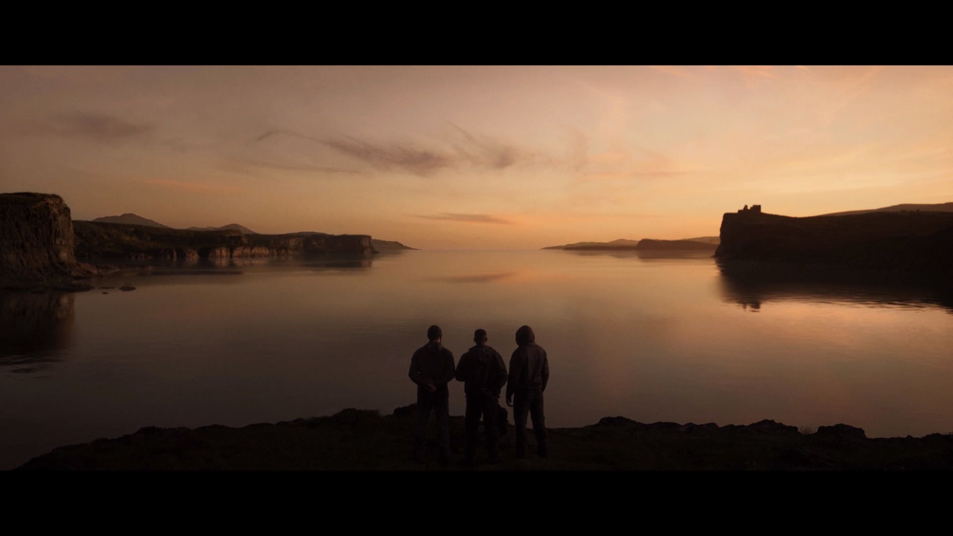 Screenshot from MW3 2023 shows 3 men standing on cliffside overlooking a large body of water with the sunsetting.