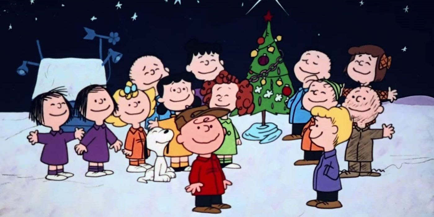 The cast of A Charlie Brown Christmas gathered outdoors around the tree smiling