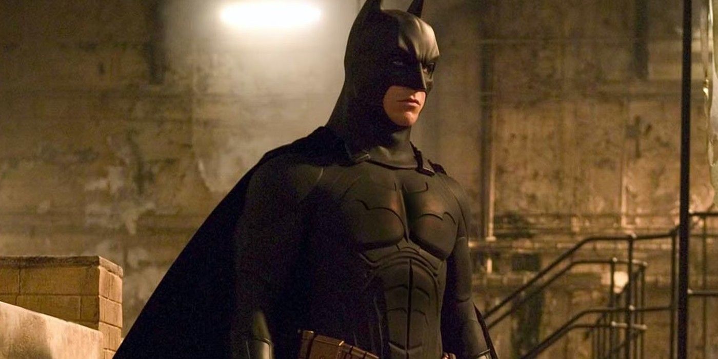 Batman (Christian Bale) stands stoically inside a warehouse as he prepares to fight some thugs in Batman Begins