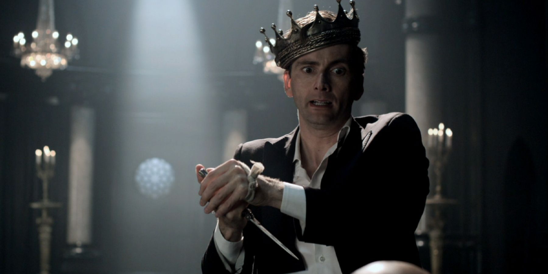 David Tennant wearing a crown and holding a knife in Hamlet.