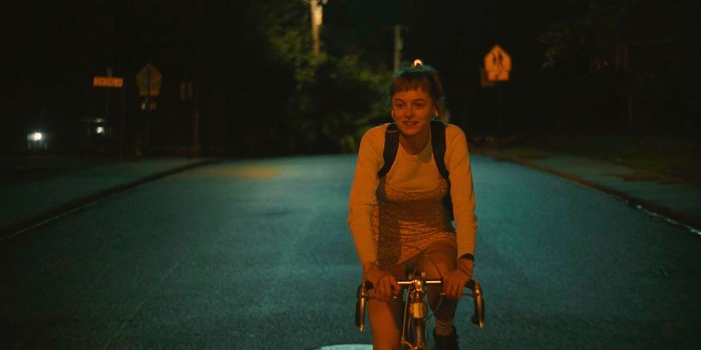 Emma Corrin as Darby bikes down a quiet road in A Murder at the End of the World