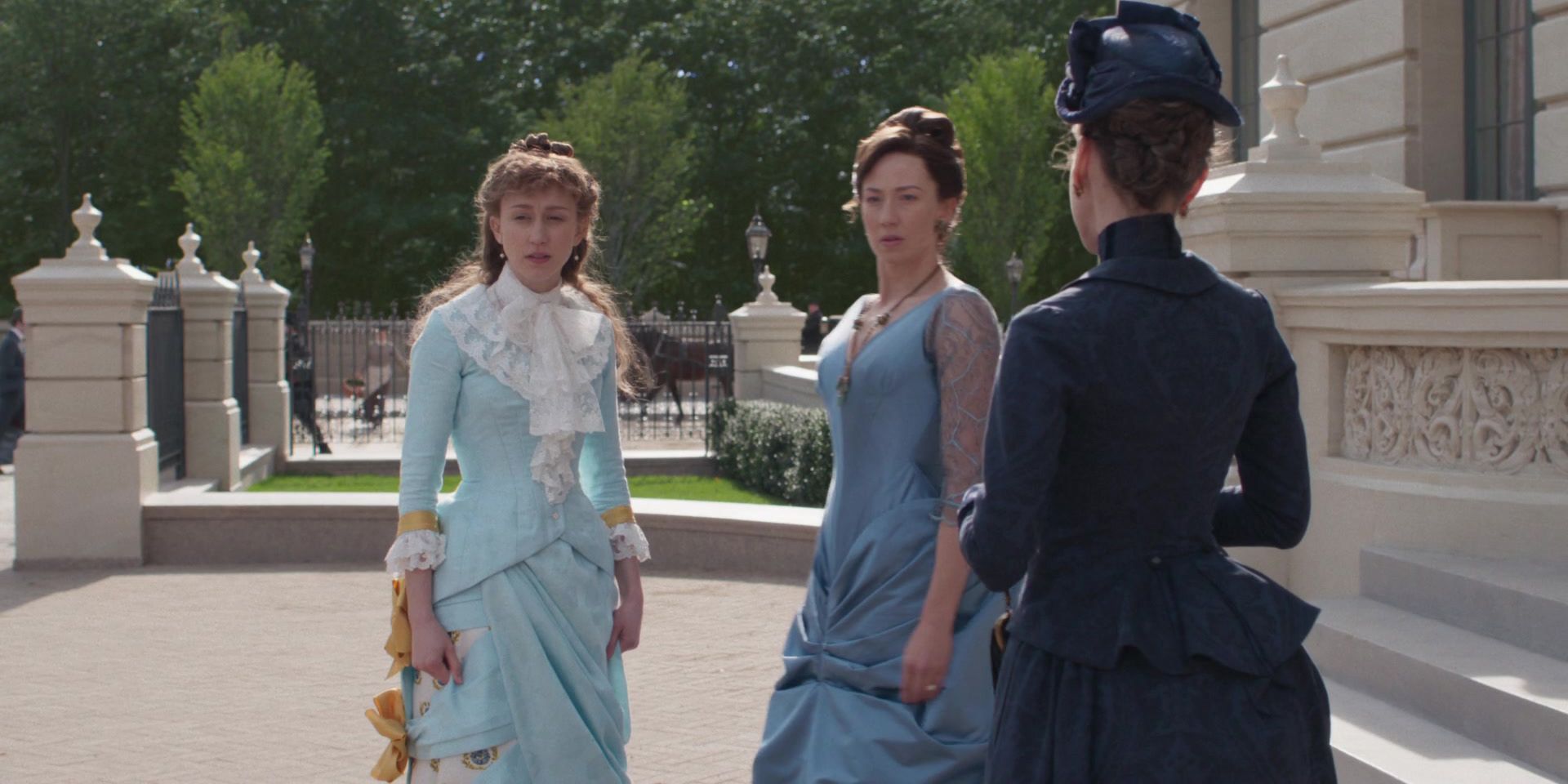 Taissa Farmiga as Gladys in The Gilded Age. She's wearing a blue dress with white embellishments and standing near other women