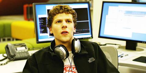 Jesse Eisenberg as Mark with his headphone around his neck and computers behind him in The Social Network