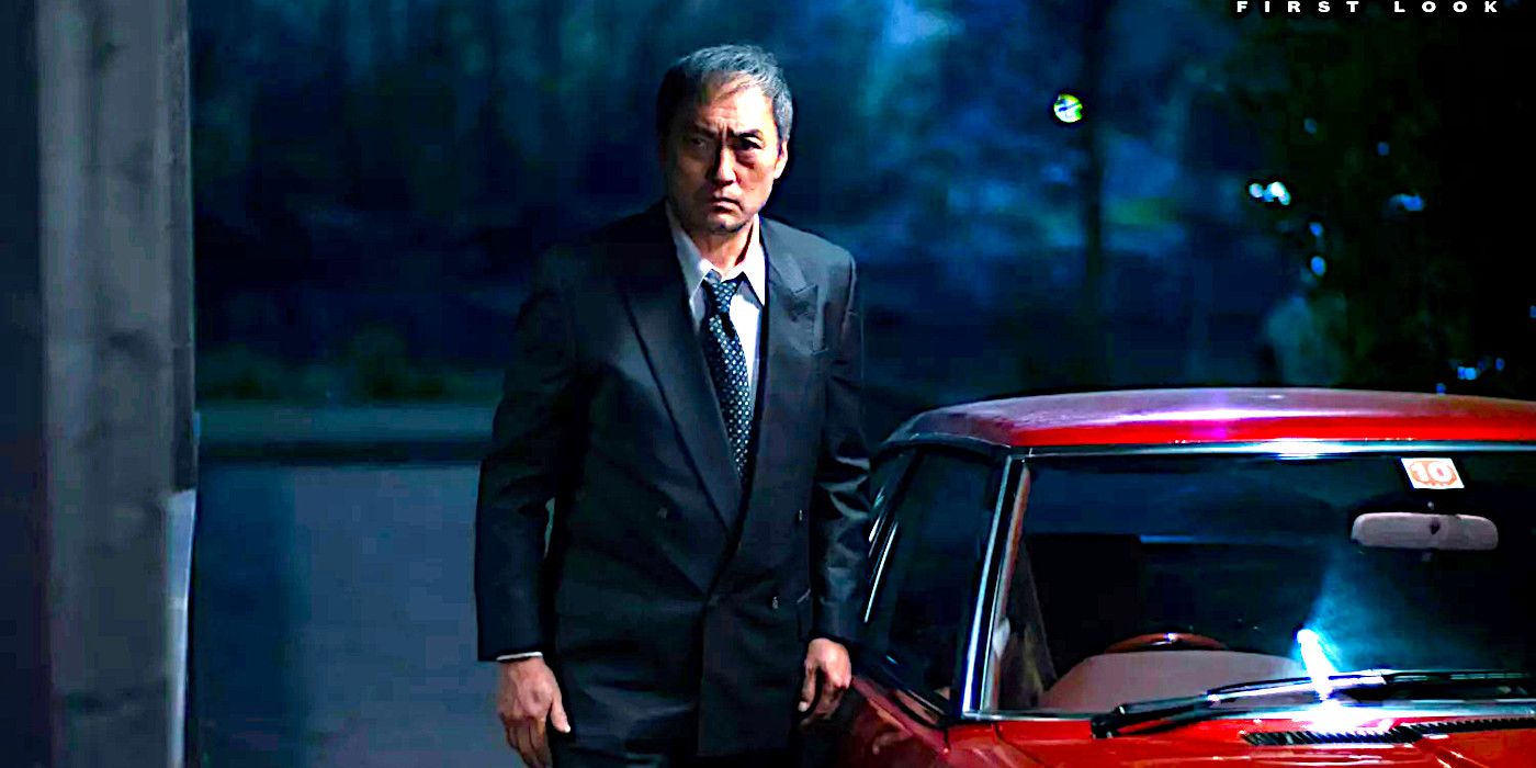Ken Watanabe peers around in a dark garage next to a red car in Tokyo Vice season 2