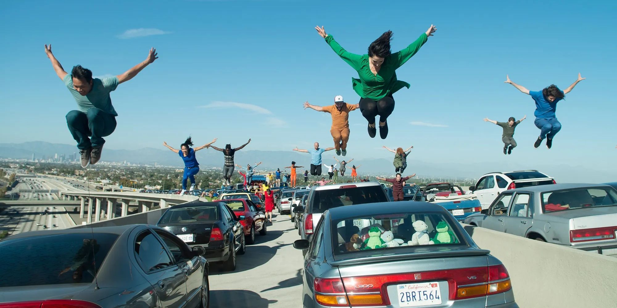 A group of dancing jumping on top of their cars on an LA freeway