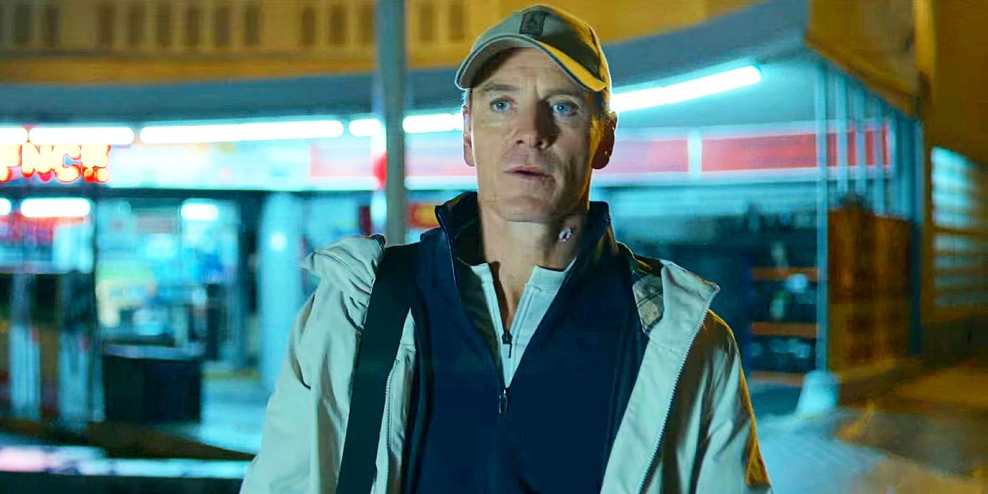 Michael Fassbender wearing a baseball cap in front of a shop in The Killer.